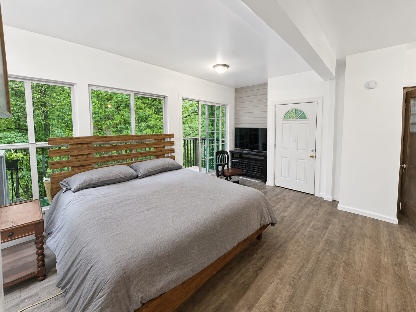 Master bedroom after editing — neutral color, coat rack and clutter removed, balcony greenery legible through the windows.