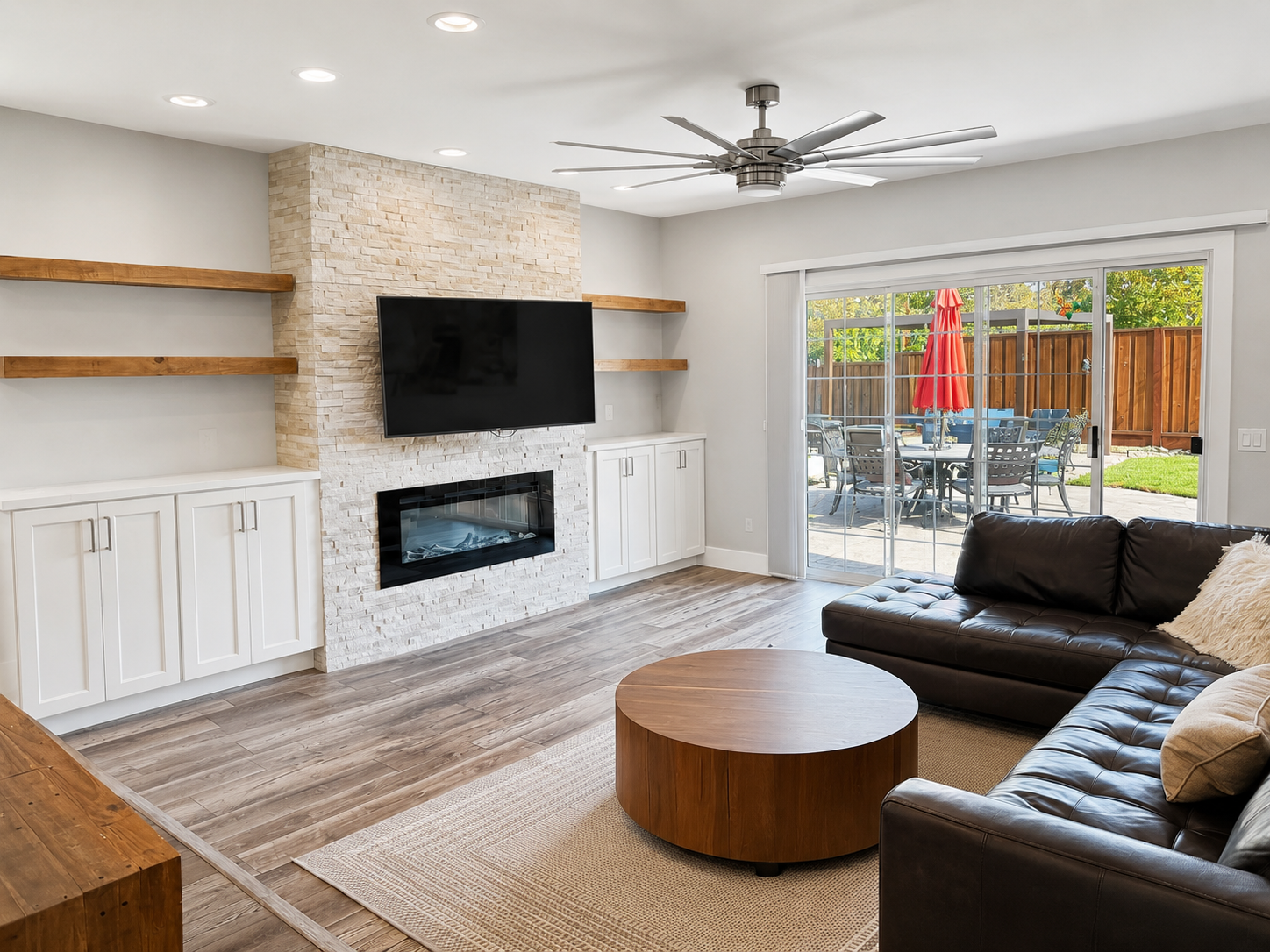 Same living room after editing — neutral whites, bean bag and art removed, patio + umbrella + dining set legible through the sliding doors.