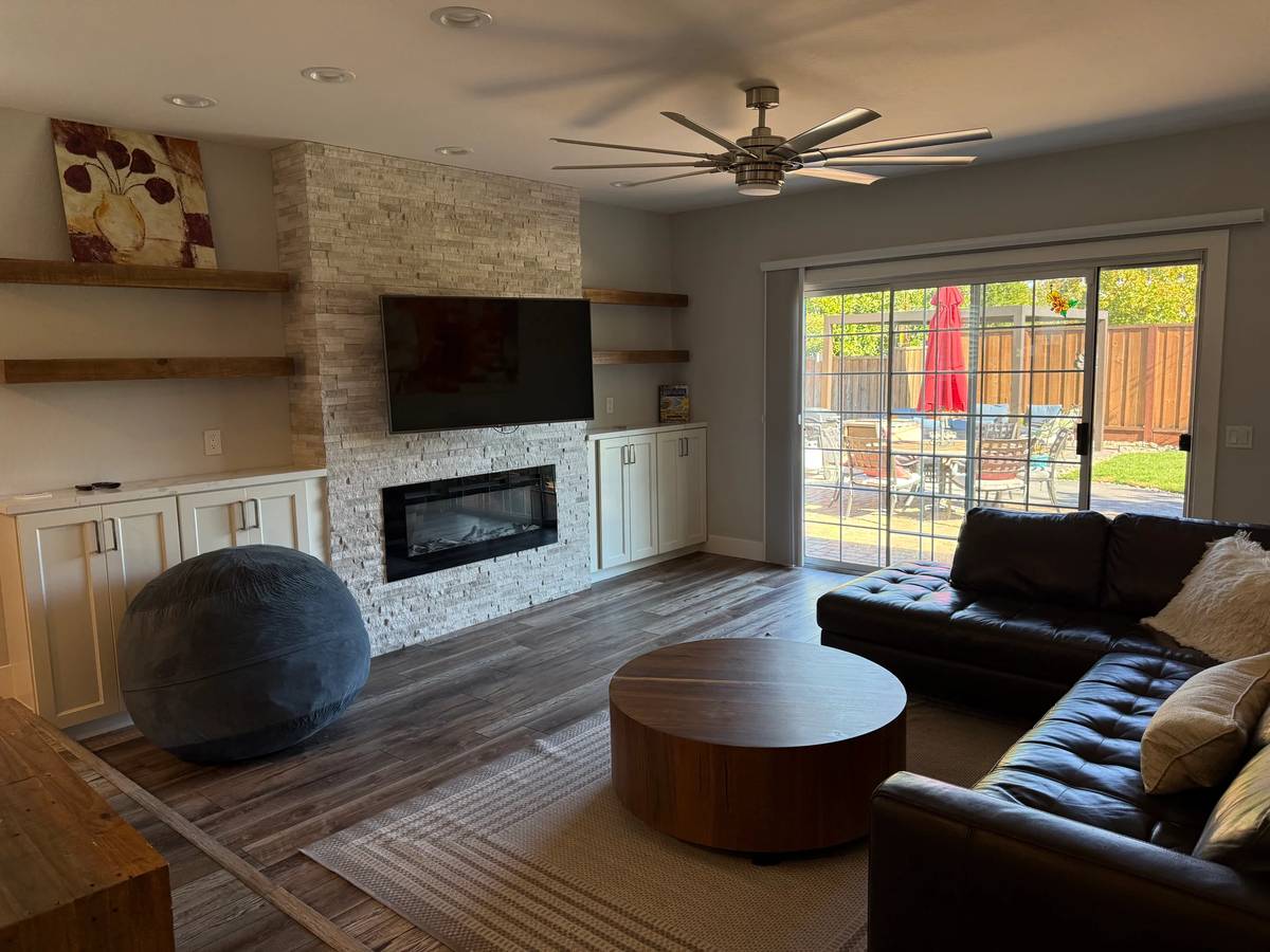 Open-plan living room before editing — warm-yellow color cast, bean bag in front of the fireplace, framed art on the left wall, blown-out patio view.