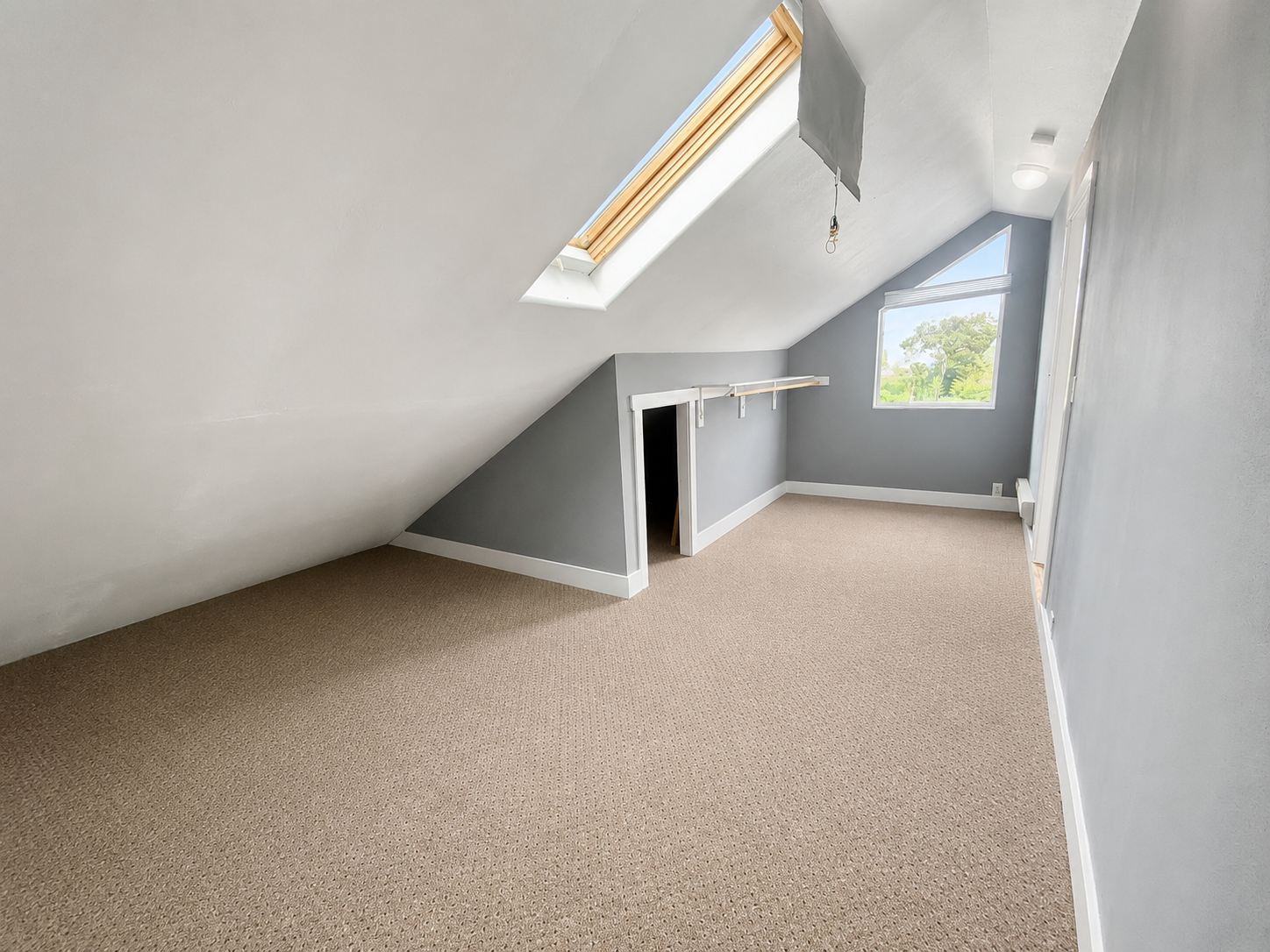 Same attic bedroom after editing — walls warmed to a true neutral grey, skylight and dormer window balanced, carpet contrast restored, room reads habitable rather than empty.
