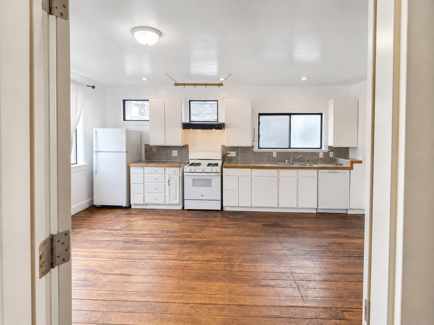 Same kitchen after editing — true white ceiling and cabinets, window detail legible, wood floor grain clean.