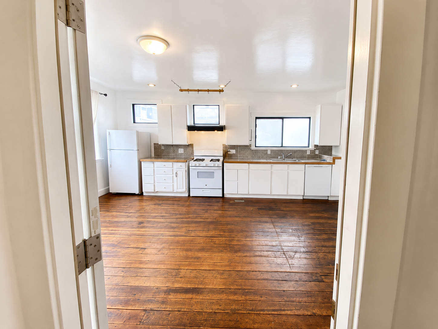 Galley kitchen before editing — warm-yellow ceiling cast, blown-out window frames, slightly orange floor tone.