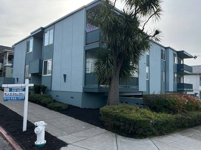 Three-story blue mid-century apartment building before editing — flat overcast sky, 'AVAILABLE FOR RENT' sign and fire hydrant in the foreground.