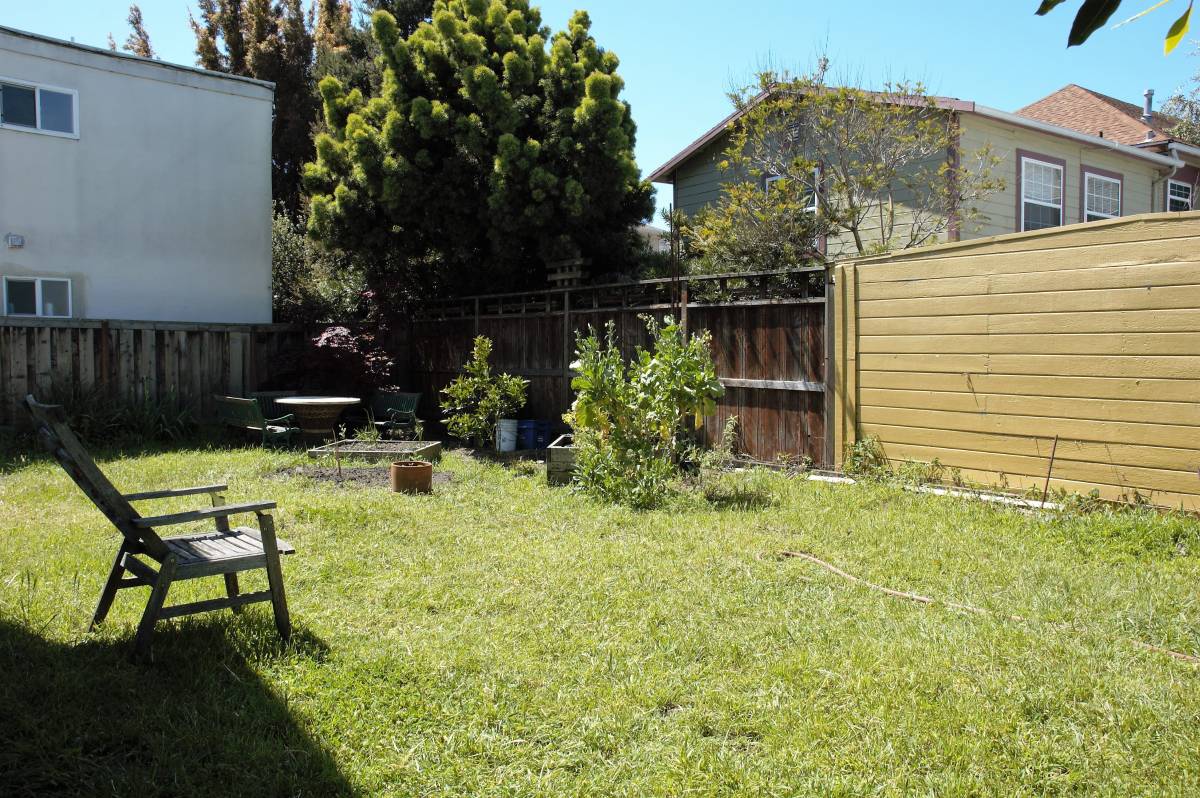 Backyard before editing — wooden Adirondack chair in the foreground, hose across the grass, patchy lawn with harsh midday shadows.